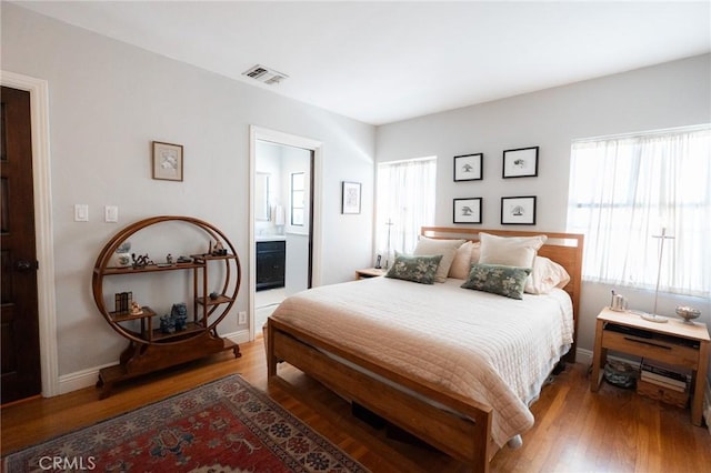 bedroom with ensuite bathroom, wood-type flooring, and multiple windows