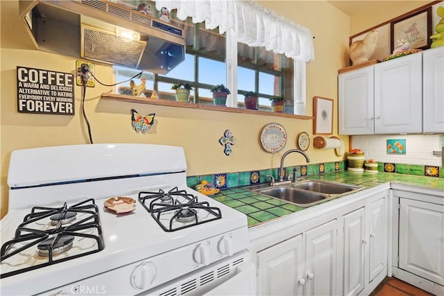 kitchen with tile counters, gas range gas stove, sink, and white cabinetry