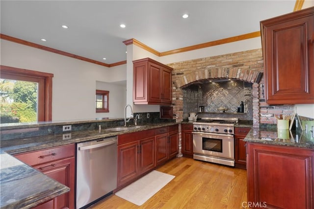 kitchen with appliances with stainless steel finishes, dark stone countertops, light hardwood / wood-style flooring, and sink