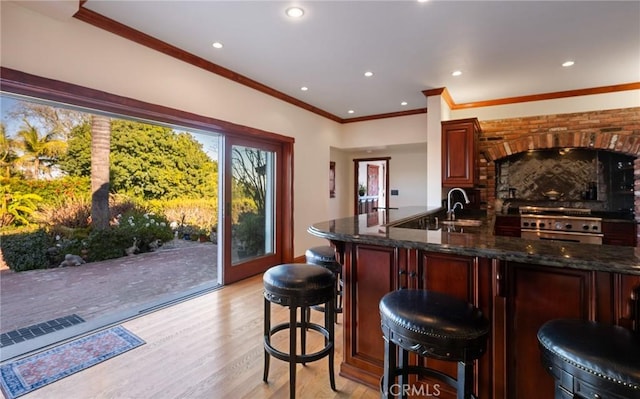 kitchen with stainless steel range, a breakfast bar area, light wood-type flooring, dark stone counters, and sink