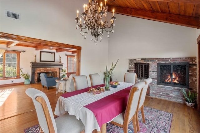 dining room featuring wooden ceiling, vaulted ceiling with beams, a brick fireplace, and light hardwood / wood-style flooring