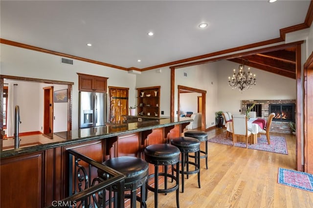 bar featuring decorative light fixtures, dark stone counters, a fireplace, stainless steel fridge, and light wood-type flooring