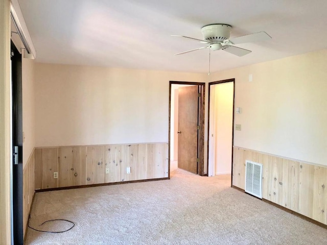 carpeted empty room featuring ceiling fan and wood walls