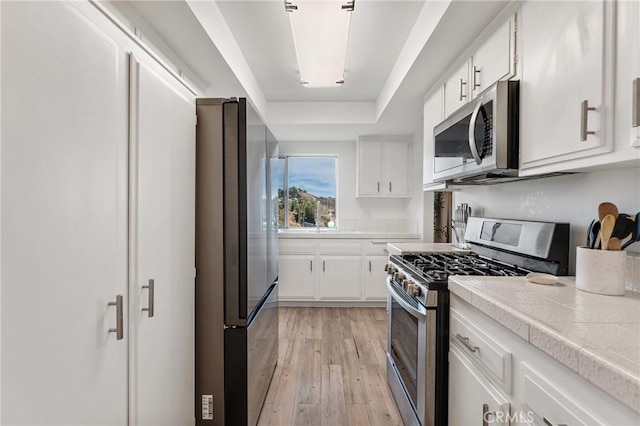 kitchen with stainless steel appliances, a raised ceiling, light hardwood / wood-style floors, and white cabinets