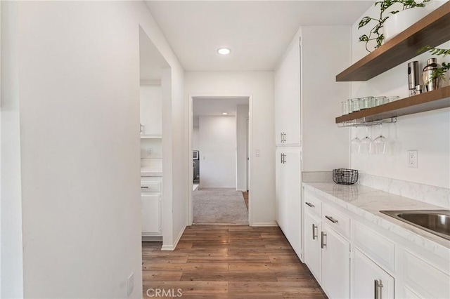 bar featuring dark wood-type flooring, sink, light stone counters, and white cabinetry