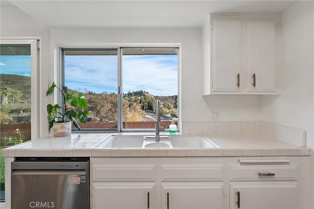 kitchen featuring stainless steel dishwasher, tile counters, sink, and white cabinetry