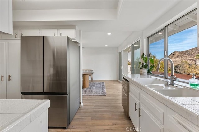 kitchen featuring appliances with stainless steel finishes, light hardwood / wood-style floors, white cabinetry, and tile counters