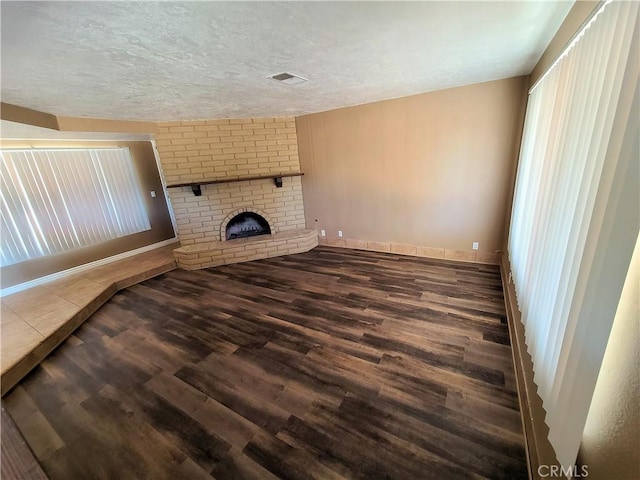 unfurnished living room featuring wood-type flooring, a brick fireplace, and a textured ceiling