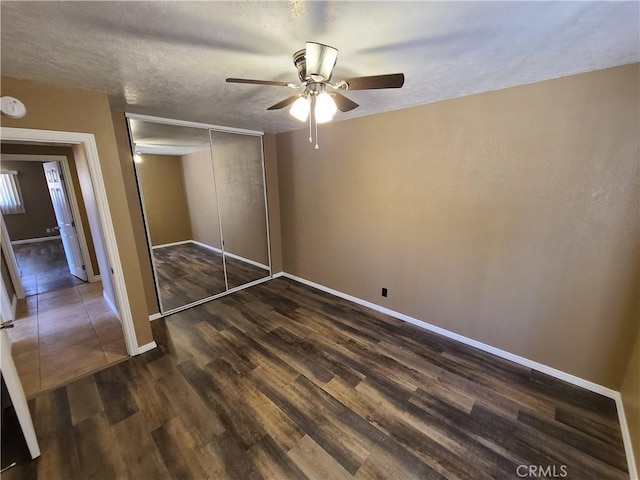 unfurnished bedroom with ceiling fan, a closet, dark hardwood / wood-style flooring, and a textured ceiling