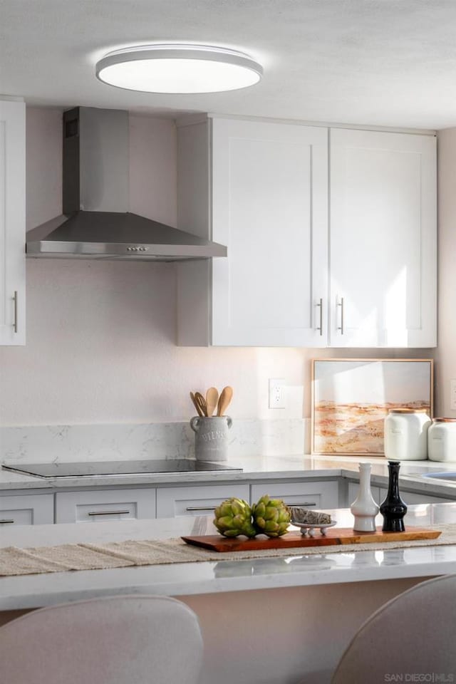 details featuring light stone countertops, wall chimney range hood, black electric stovetop, and white cabinetry