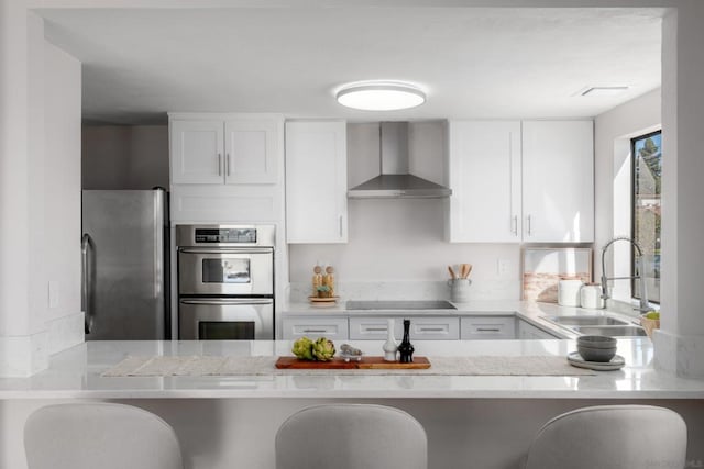 kitchen featuring a breakfast bar, white cabinetry, appliances with stainless steel finishes, and wall chimney exhaust hood