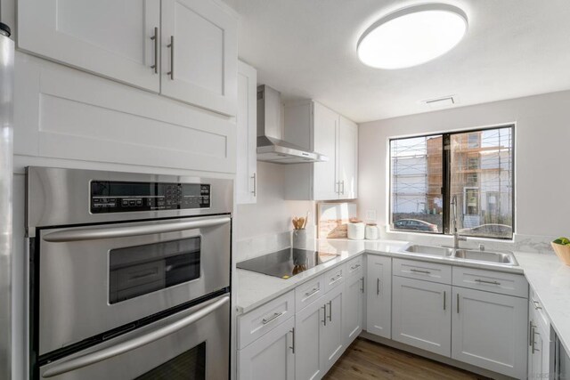 kitchen featuring sink, wall chimney range hood, white cabinets, and stainless steel double oven