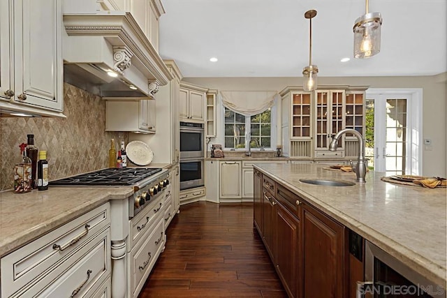 kitchen featuring custom exhaust hood, appliances with stainless steel finishes, decorative light fixtures, light stone counters, and sink