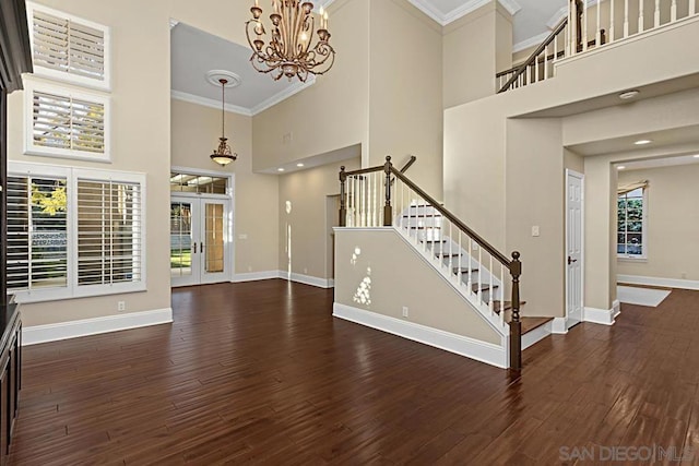 interior space featuring a notable chandelier, a high ceiling, dark wood-type flooring, ornamental molding, and french doors