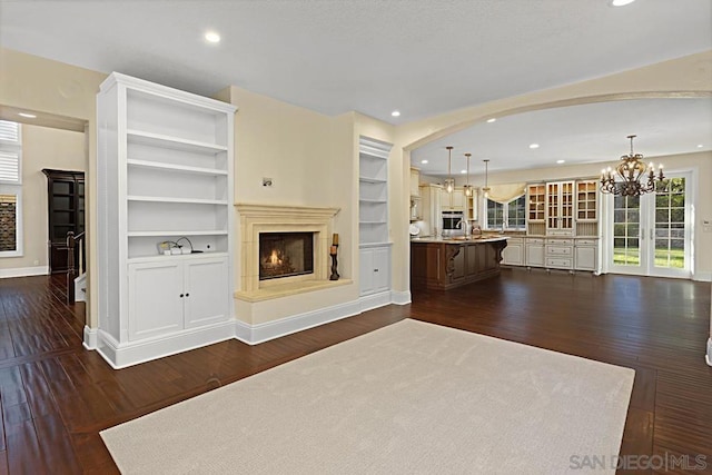 unfurnished living room with sink, built in shelves, dark hardwood / wood-style floors, and a notable chandelier