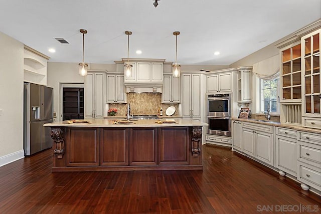 kitchen featuring pendant lighting, appliances with stainless steel finishes, tasteful backsplash, dark hardwood / wood-style floors, and a center island with sink