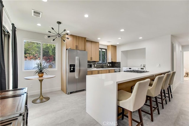 kitchen featuring kitchen peninsula, a kitchen bar, decorative backsplash, an inviting chandelier, and stainless steel appliances