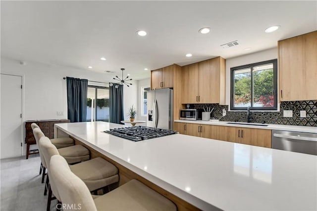 kitchen featuring backsplash, a notable chandelier, sink, appliances with stainless steel finishes, and a kitchen breakfast bar