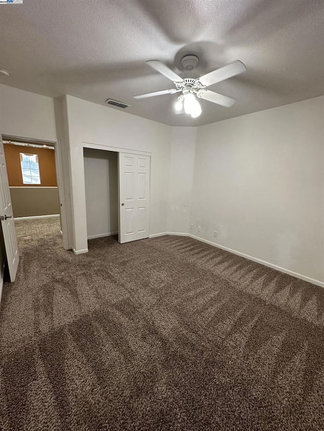 unfurnished bedroom with ceiling fan, dark carpet, a closet, and a textured ceiling