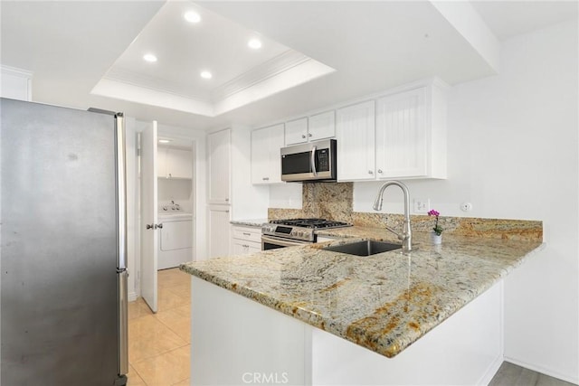 kitchen with washer / clothes dryer, white cabinetry, stainless steel appliances, sink, and a raised ceiling