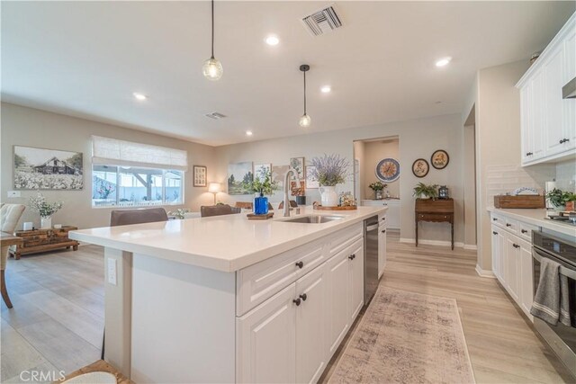 kitchen featuring a center island with sink, stainless steel appliances, hanging light fixtures, white cabinets, and sink