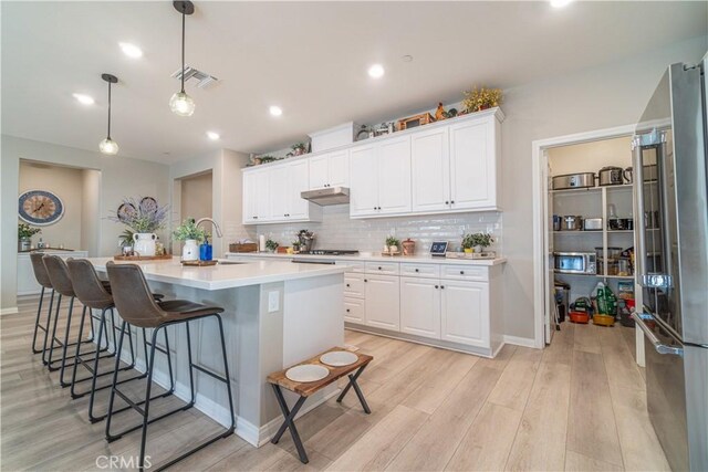 kitchen with decorative light fixtures, white cabinets, stainless steel appliances, and a kitchen island with sink