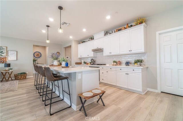 kitchen with pendant lighting, white cabinetry, sink, a kitchen island with sink, and light wood-type flooring