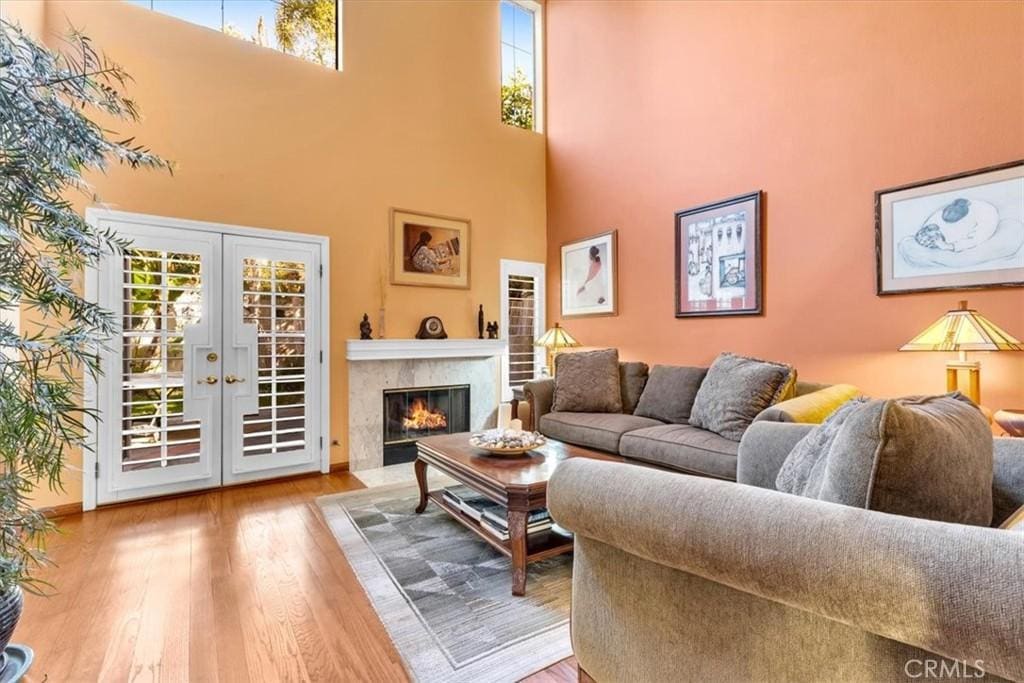 living room with light hardwood / wood-style floors, french doors, a towering ceiling, and a fireplace