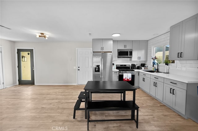 kitchen with tasteful backsplash, sink, light hardwood / wood-style flooring, appliances with stainless steel finishes, and gray cabinetry