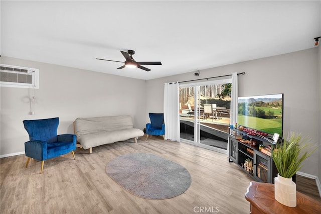 living area featuring a wall unit AC, ceiling fan, and light hardwood / wood-style floors