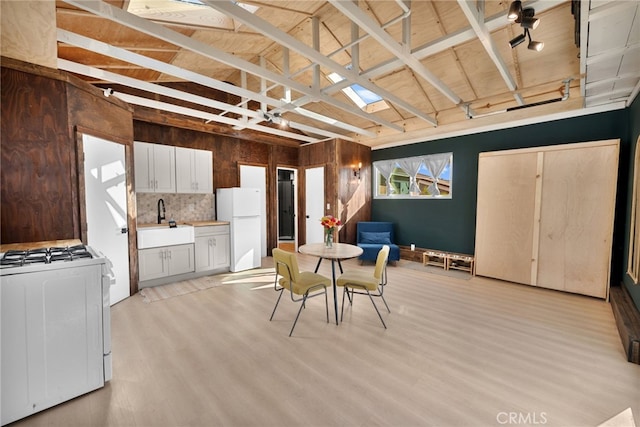 dining area featuring vaulted ceiling with beams, sink, track lighting, and light hardwood / wood-style flooring