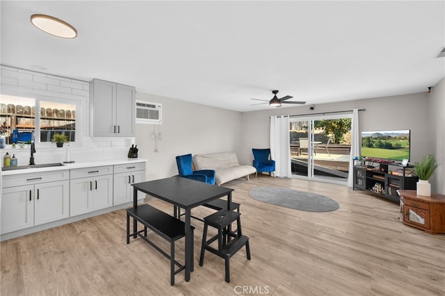 dining area with ceiling fan, sink, light hardwood / wood-style flooring, and a wall unit AC