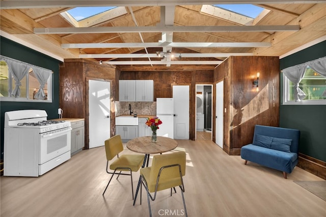 dining room featuring sink, light hardwood / wood-style floors, wood walls, and lofted ceiling with beams