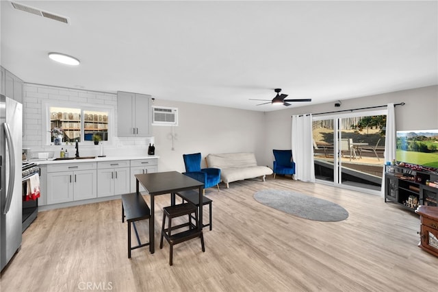 dining room with ceiling fan, an AC wall unit, sink, and light hardwood / wood-style floors