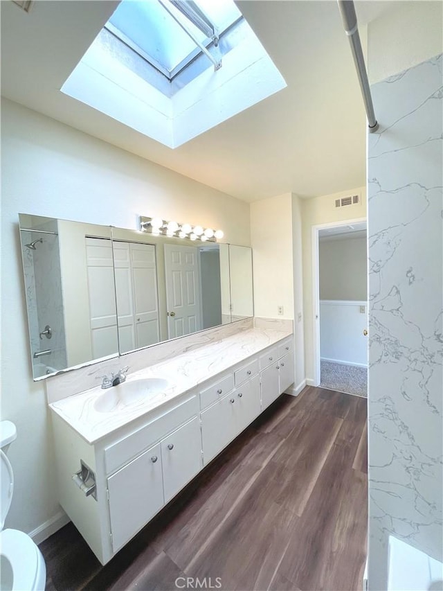 bathroom with toilet, a skylight, hardwood / wood-style floors, and vanity