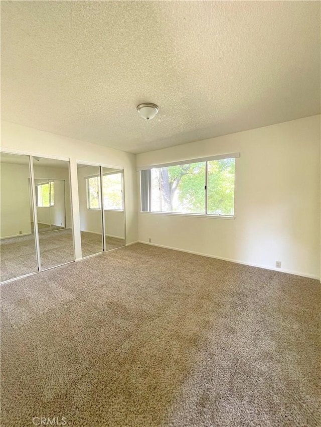 unfurnished bedroom featuring carpet floors, two closets, and a textured ceiling