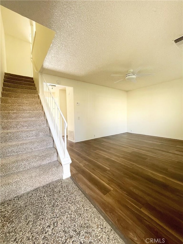 staircase with a textured ceiling, ceiling fan, and hardwood / wood-style flooring