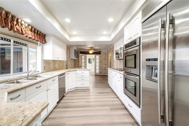 kitchen featuring stainless steel appliances, a tray ceiling, light stone countertops, white cabinets, and sink