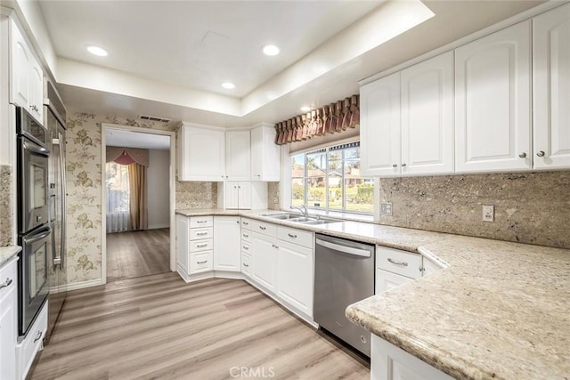 kitchen with a tray ceiling, light hardwood / wood-style flooring, appliances with stainless steel finishes, white cabinets, and light stone counters