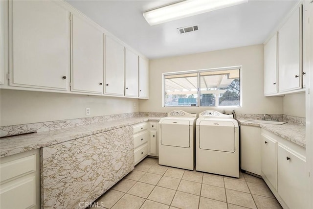 laundry area with light tile patterned floors, sink, separate washer and dryer, and cabinets