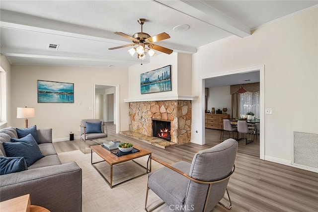 living room featuring ceiling fan, hardwood / wood-style flooring, a stone fireplace, and lofted ceiling with beams