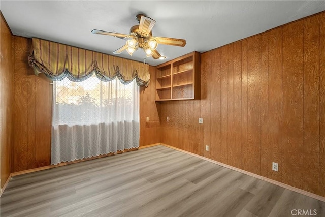 spare room with ceiling fan, wood-type flooring, and wood walls