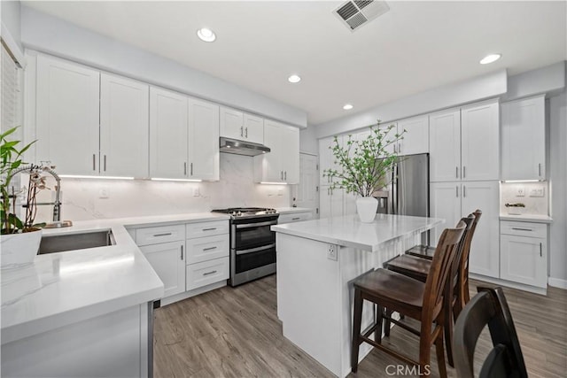 kitchen featuring sink, backsplash, stainless steel appliances, a center island, and white cabinets