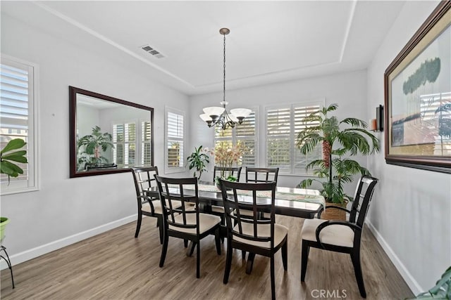 dining area with a notable chandelier, a tray ceiling, and hardwood / wood-style floors