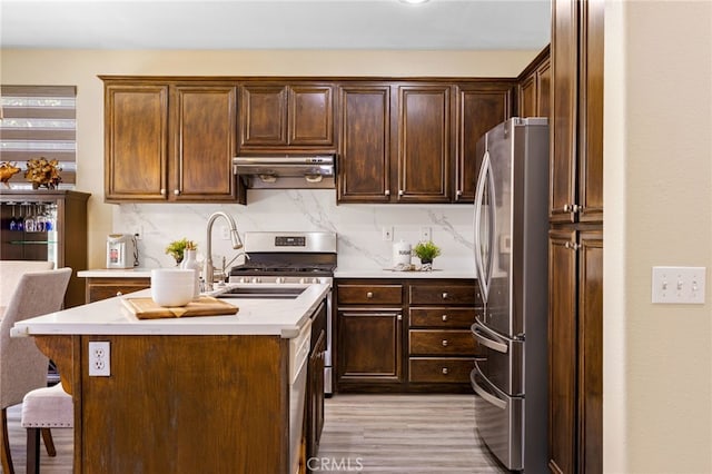 kitchen featuring a kitchen bar, an island with sink, light wood-type flooring, stainless steel refrigerator, and sink