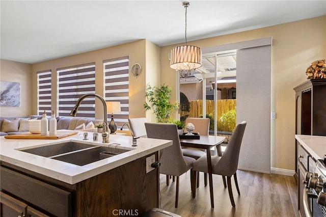 kitchen featuring stainless steel stove, pendant lighting, sink, light wood-type flooring, and dark brown cabinets