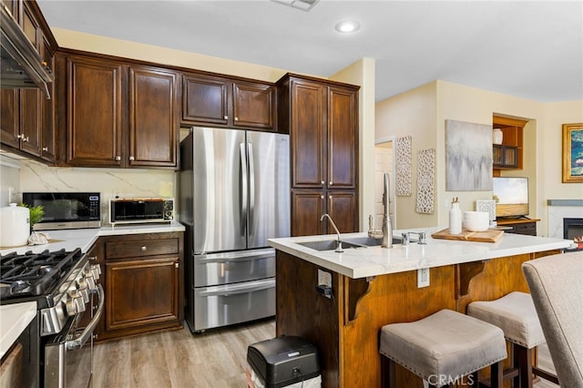 kitchen featuring light hardwood / wood-style floors, a breakfast bar, dark brown cabinetry, a kitchen island with sink, and appliances with stainless steel finishes