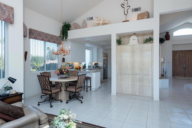 tiled dining area featuring a notable chandelier, sink, and high vaulted ceiling