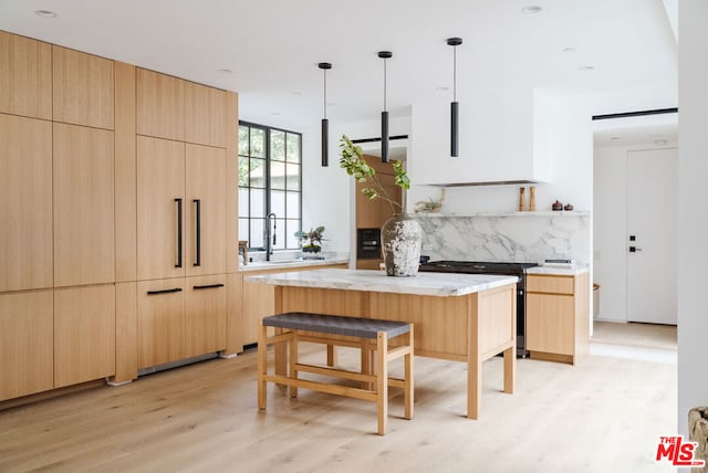 kitchen featuring light wood-type flooring, light brown cabinetry, hanging light fixtures, a kitchen island, and sink