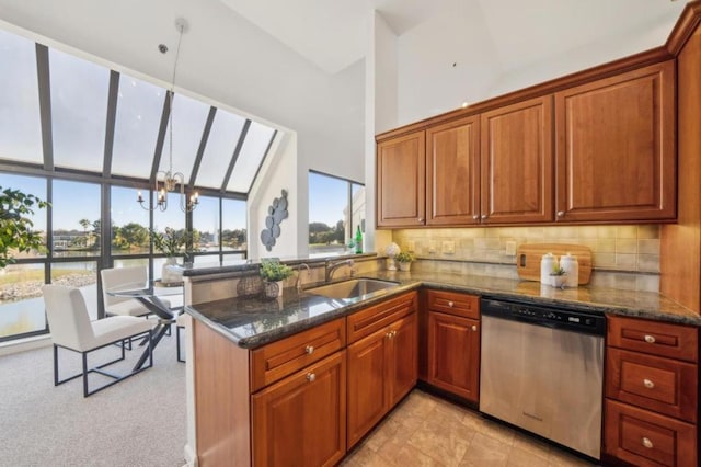 kitchen featuring kitchen peninsula, dark stone counters, a chandelier, stainless steel dishwasher, and sink